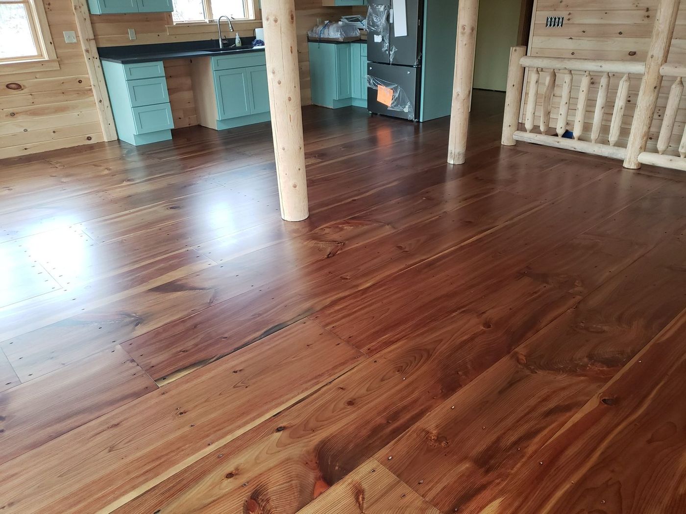 Finished wide pine floor in a warm reddish brown running through an open log home