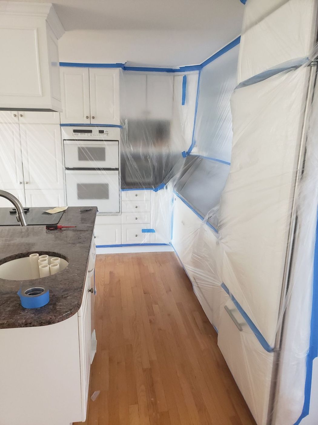 Kitchen cabinets, ovens, and refrigerator wrapped in plastic and tape before floor sanding