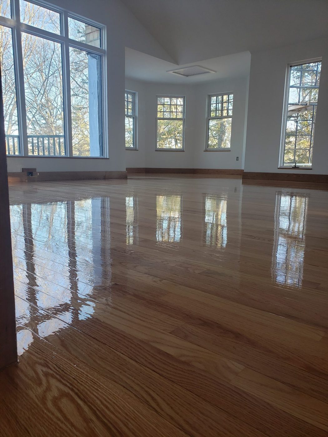 Glossy natural oak floor in a bright vaulted room with a bay of windows