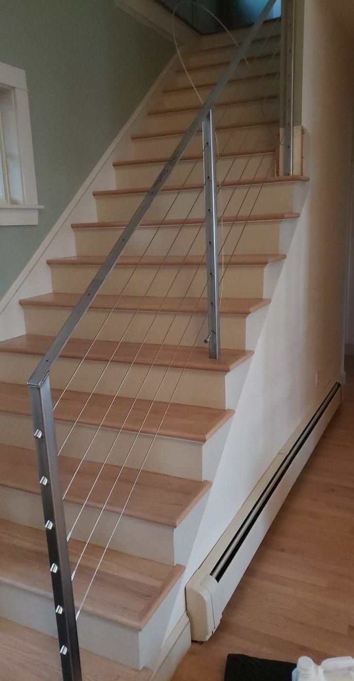Light oak stair treads with white risers beside a steel cable railing