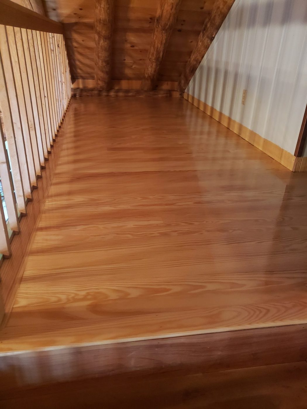 Glossy amber southern yellow pine floor in a loft with a railing and log rafters